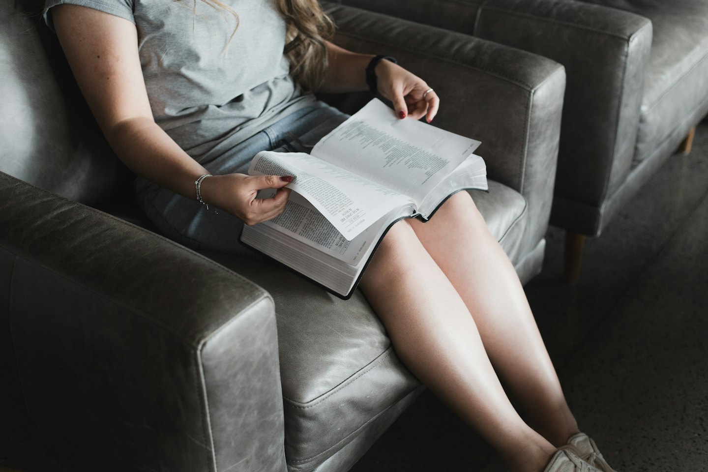 Una persona seduta su una poltrona grigia legge un grosso libro.