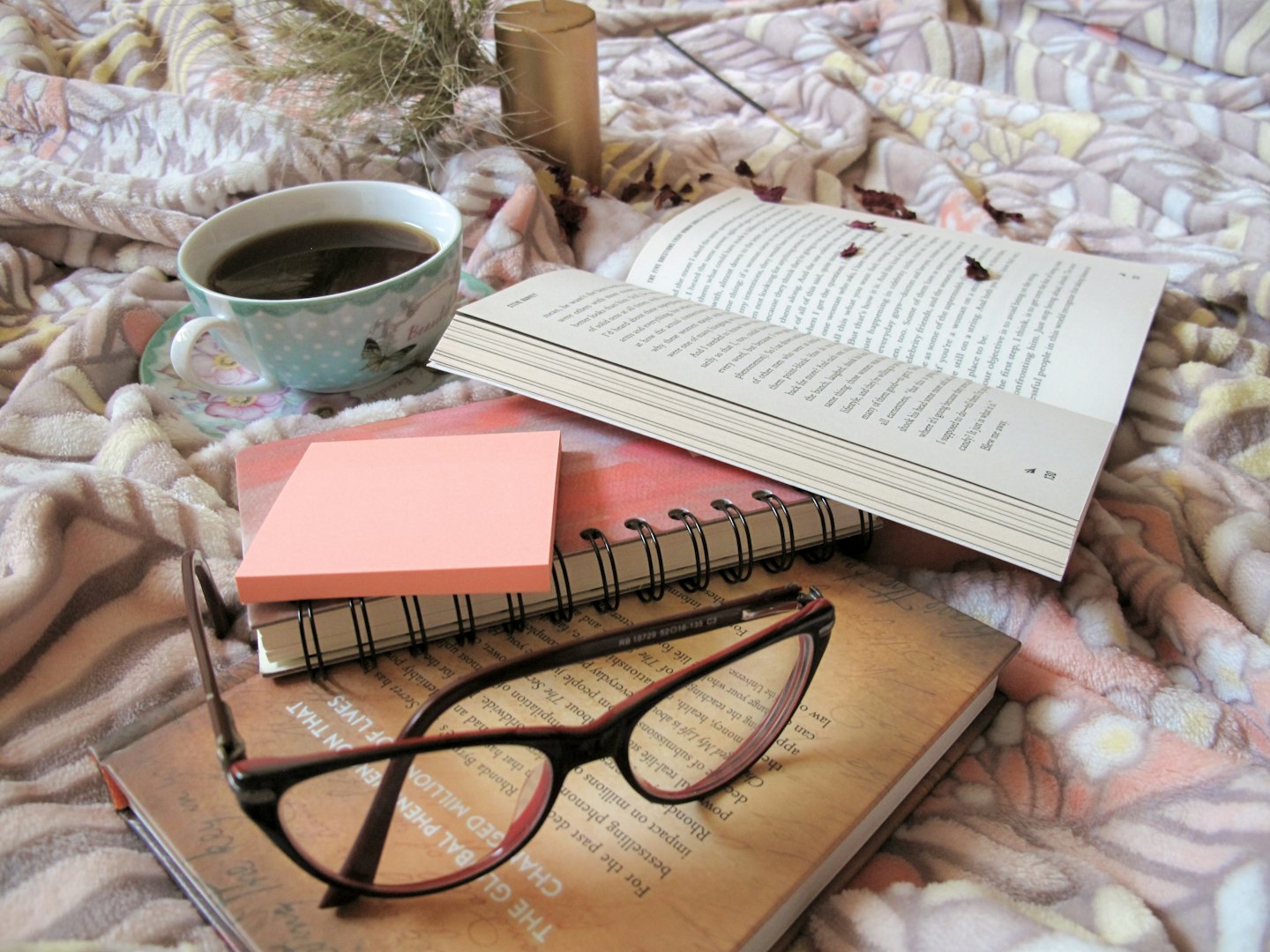 Libro aperto, caffè e occhiali su una coperta fantasia.