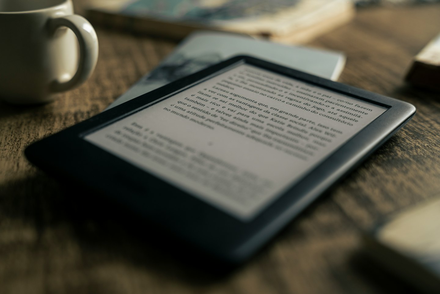 Un e-reader nero è appoggiato su un tavolo di legno scuro.