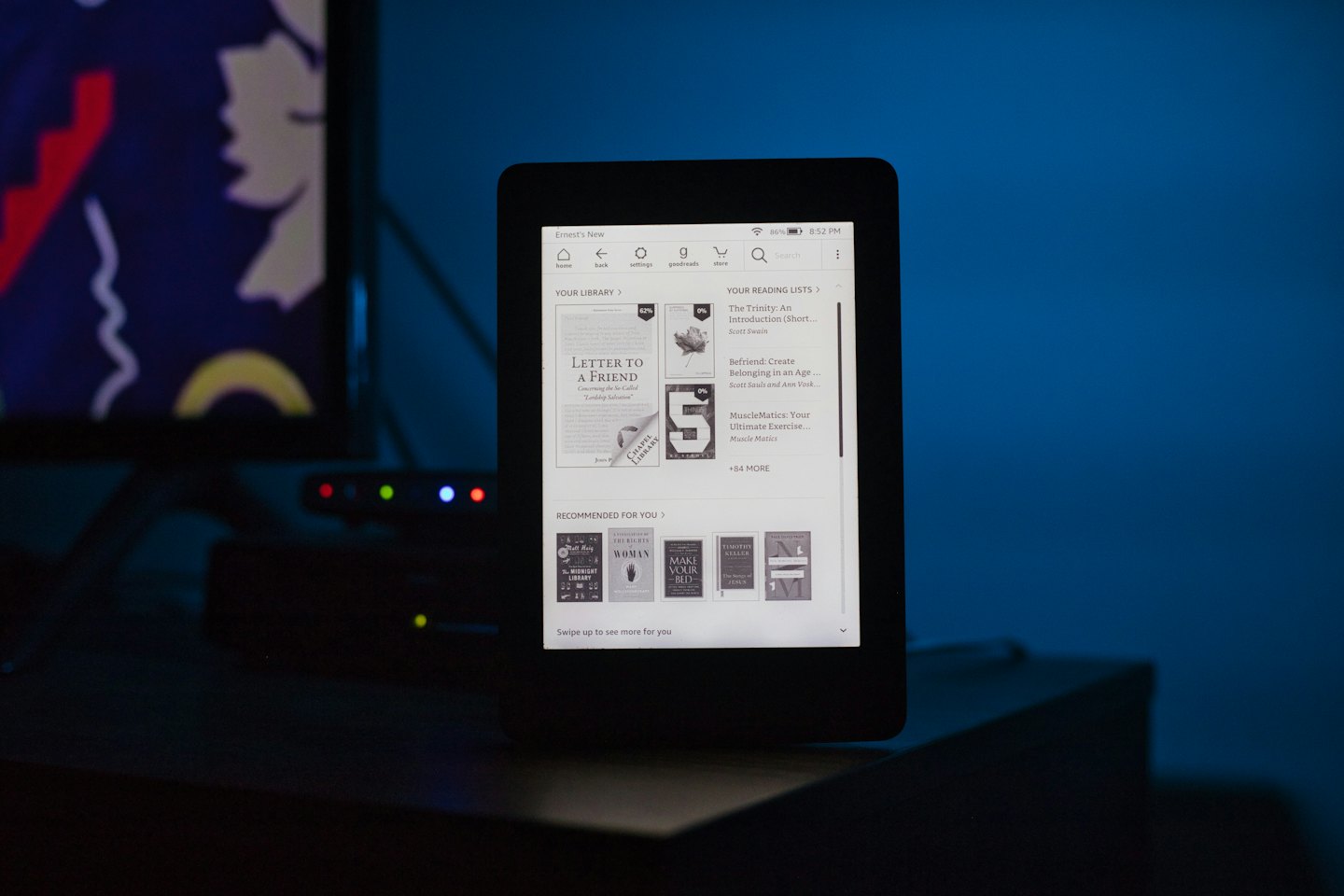 E-reader nero con copertine di libri su legno scuro.